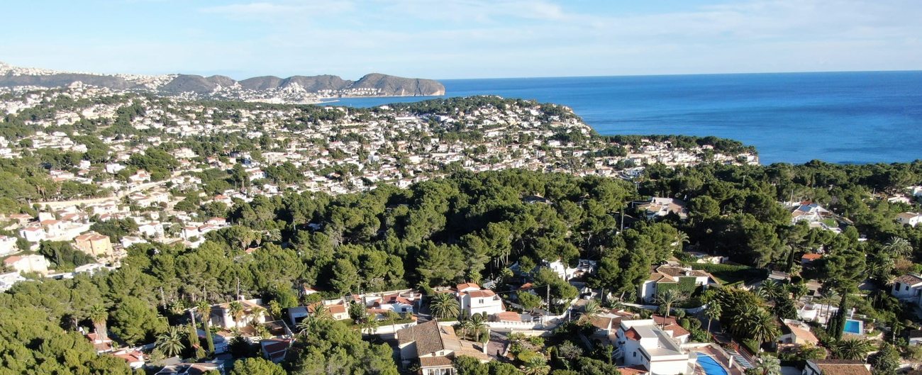 De kuststrook van Benissa, met woningen tussen de pijnbomen en in de verte de kaap bij Moraira