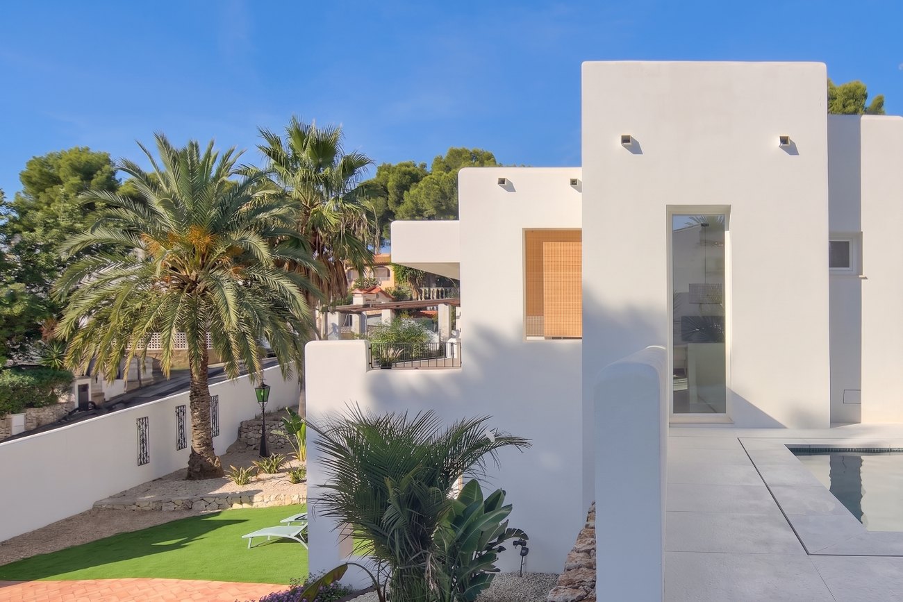 Casa Eucaliptus — fachada lateral con piscina, palmeras y el muro blanco del jardín