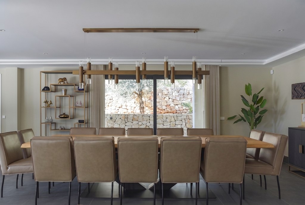 Casa Mos — comedor con mesa larga y vista al muro de piedra natural
