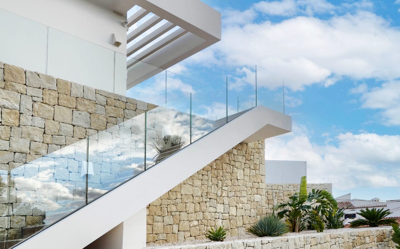 Villa El Portet — escalera exterior con barandilla de vidrio junto al muro de piedra natural