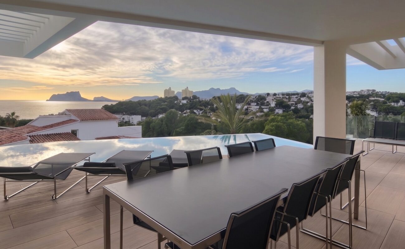 Villa El Portet — terraza cubierta con mesa, piscina desbordante y vista sobre la bahía